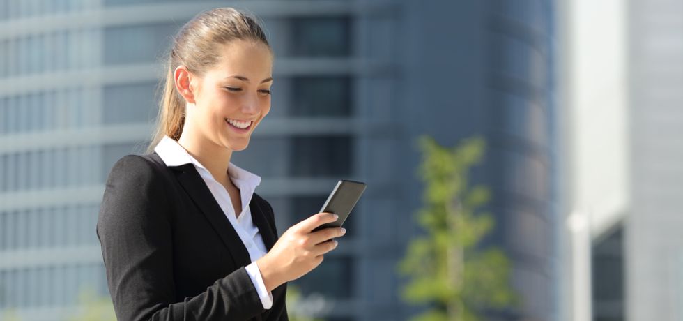 Beautiful woman with a mobile phone in the street reading text message with office buildings in the background