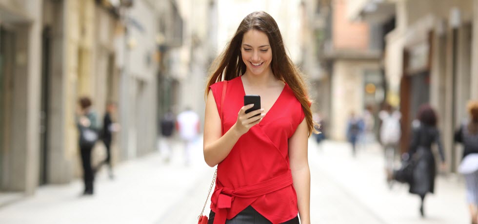 Happy woman walking in the street with mobile phone