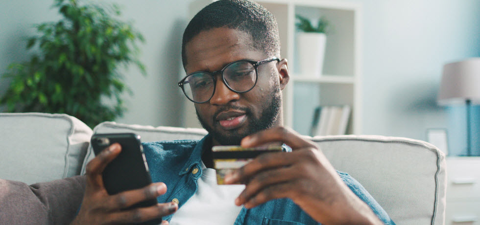 young man in glasses shopping online with credit card using smart phone at home